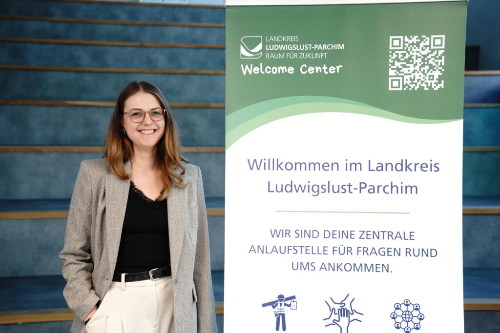 Projektmanagerin der Wifög Südwestmecklenburg, Lina Hauke, neben dem Roll Up für das Welcome Center.