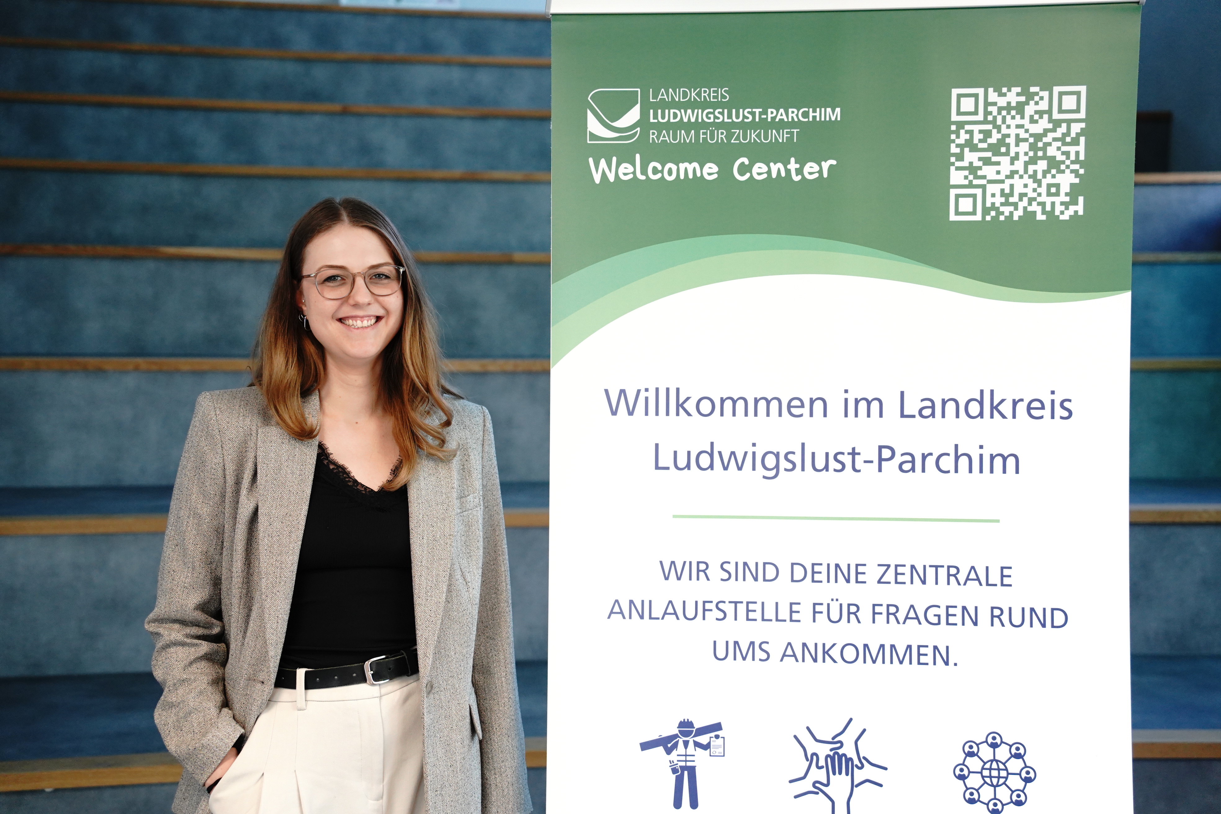 Projektmanagerin der Wifög Südwestmecklenburg, Lina Hauke, neben dem Roll Up für das Welcome Center.